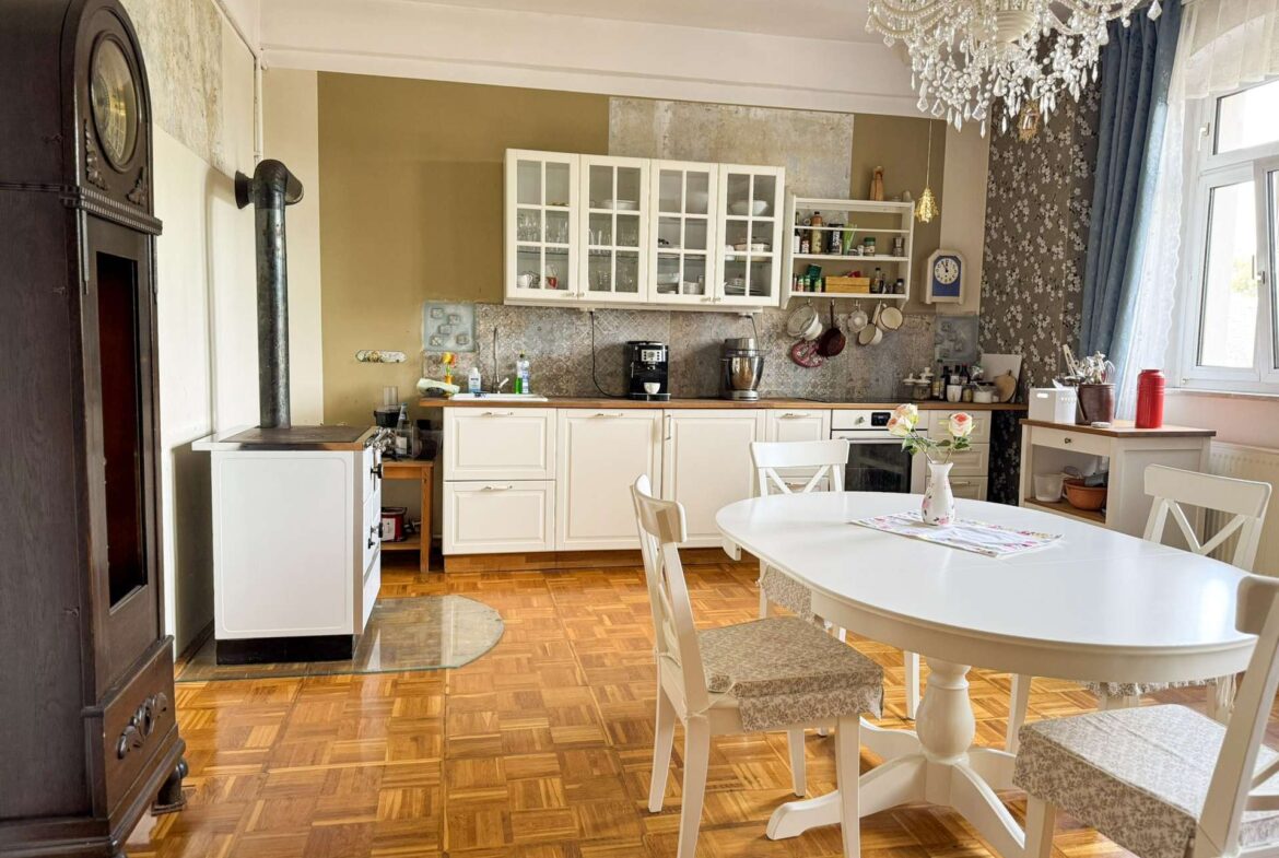 Vintage-style kitchen with white cabinets, glass-front cupboards, and a crystal chandelier above a white dining table.