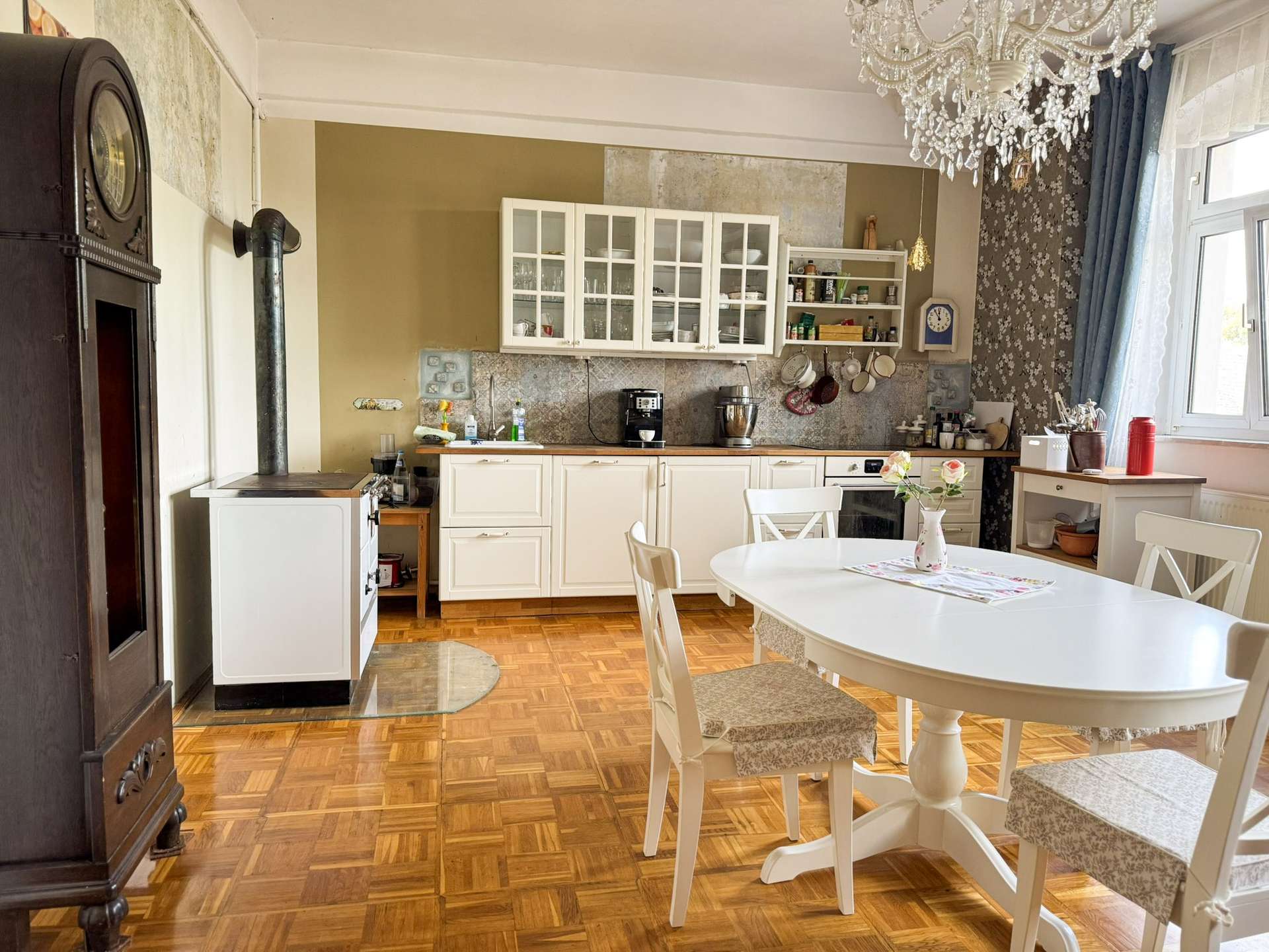 Vintage-style kitchen with white cabinets, glass-front cupboards, and a crystal chandelier above a white dining table.