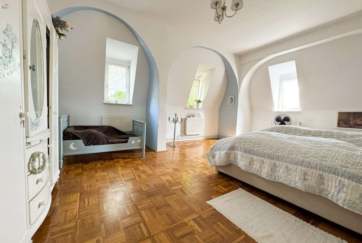 Bright bedroom with curved arches, a large bed on the right, a blue daybed on the left, and a chandelier overhead.