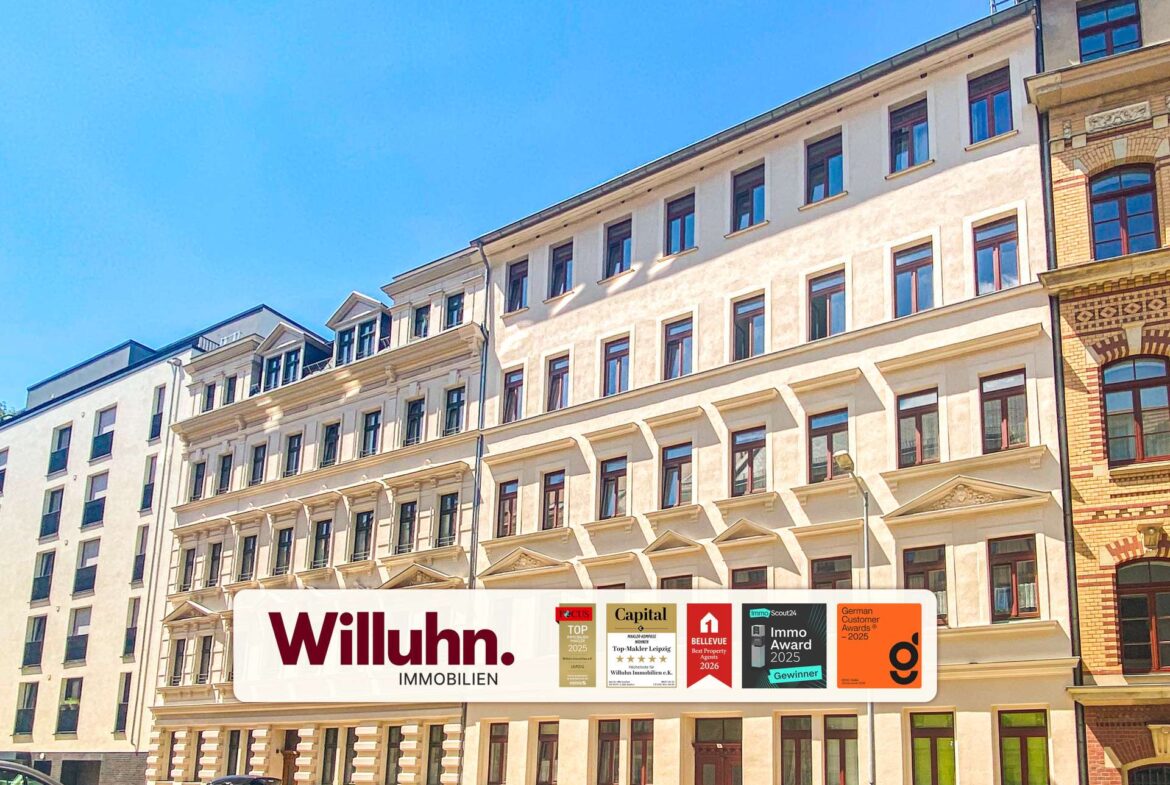 Facade of a light-colored apartment building with a large Willuhn. Immobilien banner and award logos at street level.