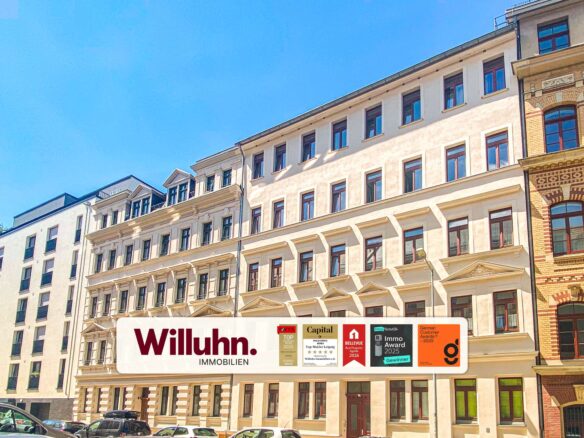 Facade of a light-colored apartment building with a large Willuhn. Immobilien banner and award logos at street level.