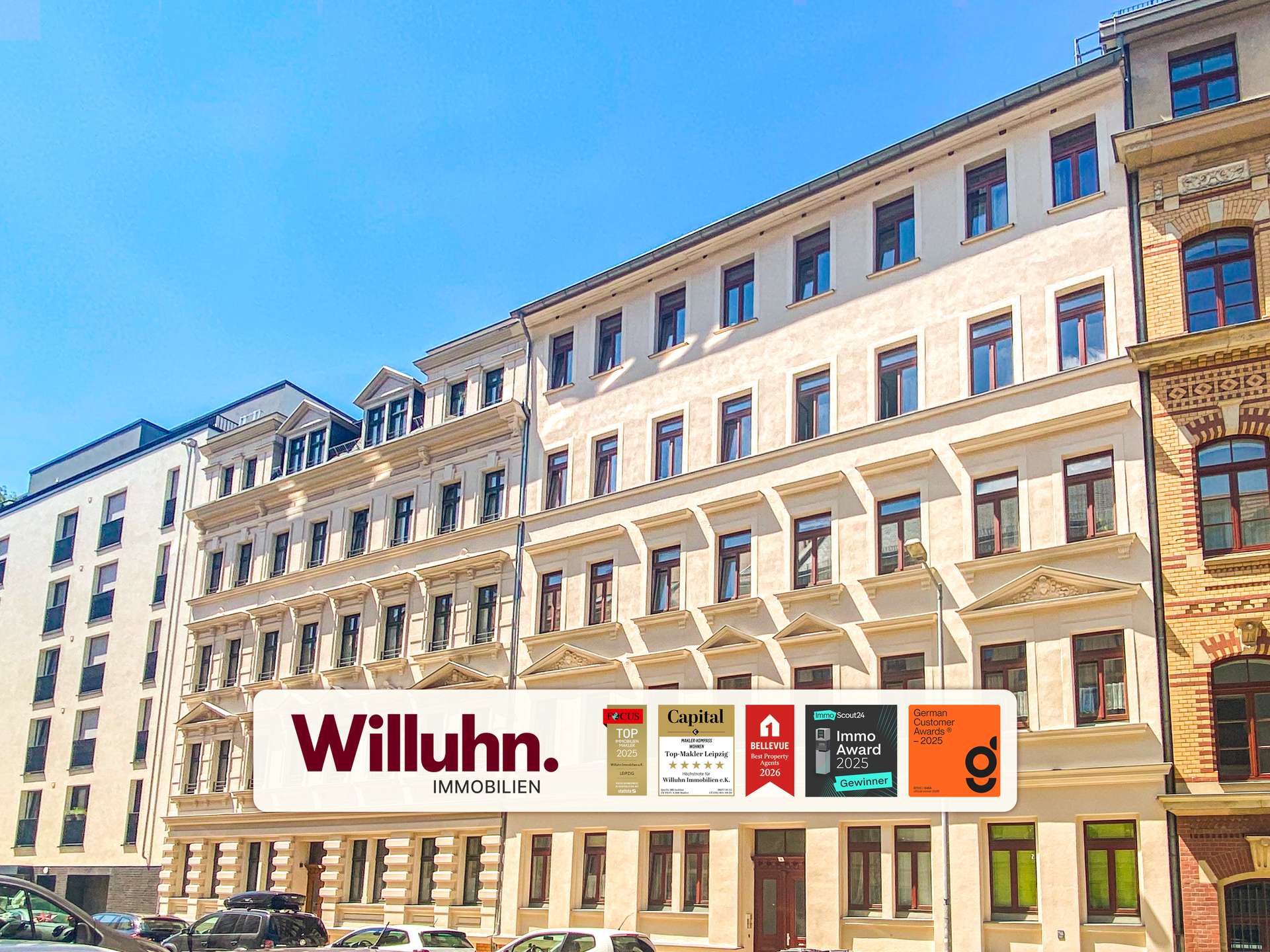 Facade of a light-colored apartment building with a large Willuhn. Immobilien banner and award logos at street level.