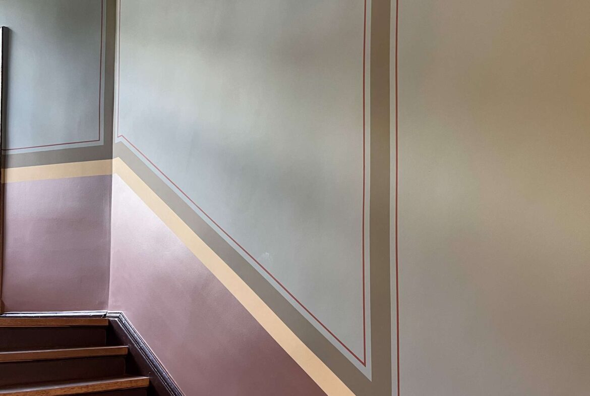 Stairwell corner with decorative wall panels featuring red-trimmed geometric frames and layered horizontal color bands in purple, gray, and beige.