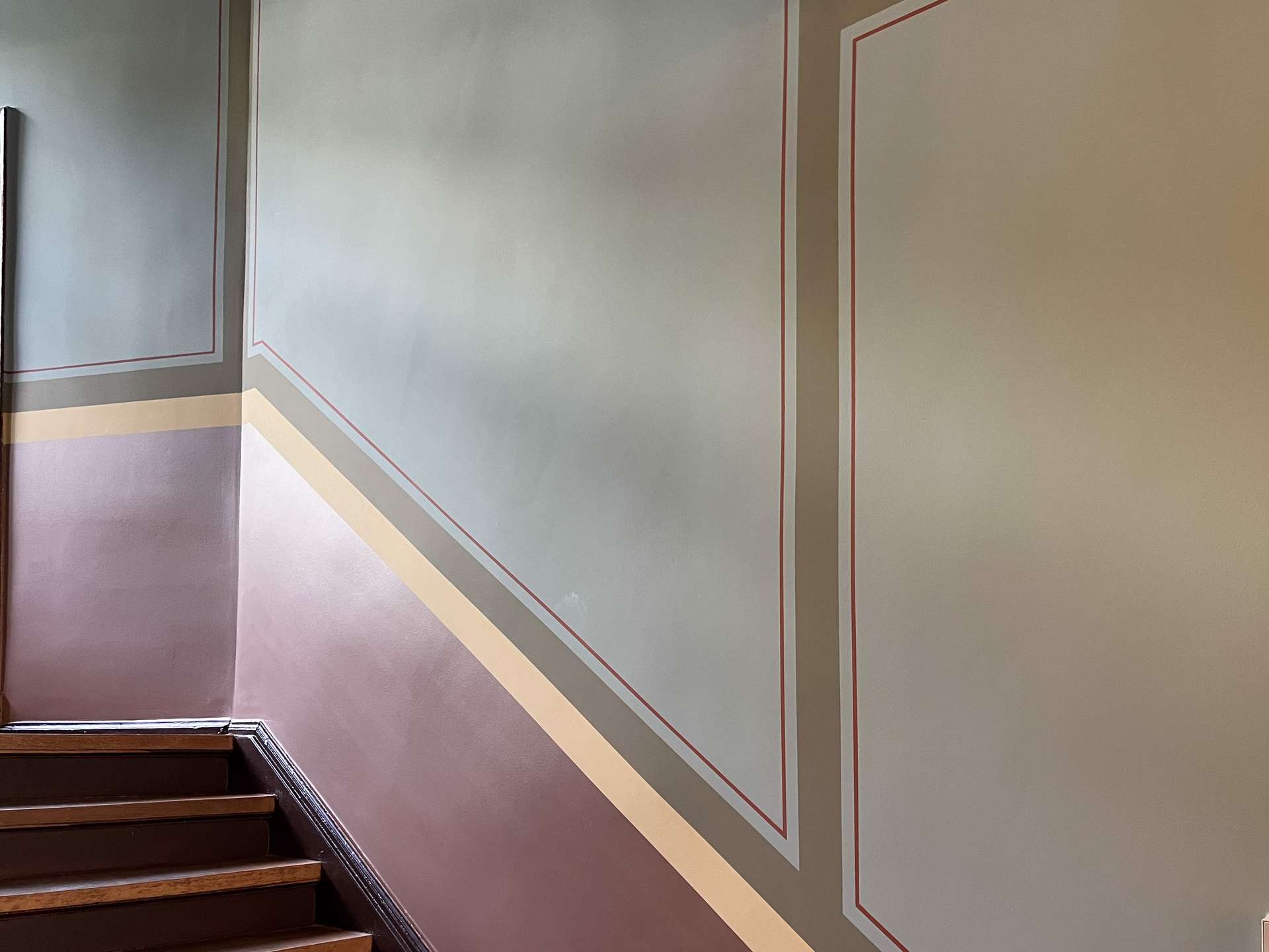 Stairwell corner with decorative wall panels featuring red-trimmed geometric frames and layered horizontal color bands in purple, gray, and beige.