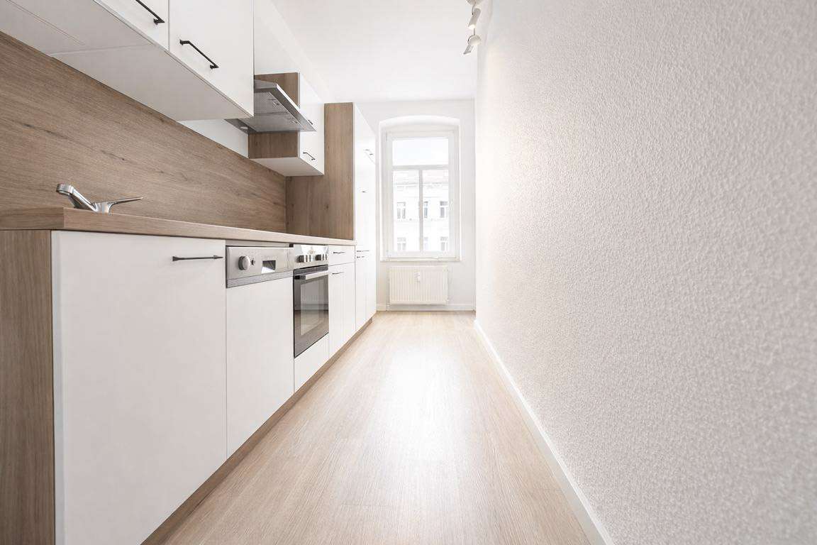 Bright narrow galley kitchen with white cabinets, wood countertops, and a window at the far end for natural light.
