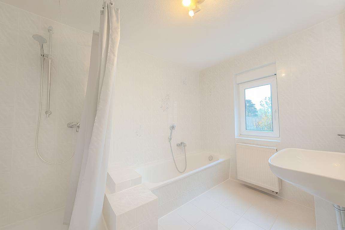 Bright white bathroom with a bathtub, separate shower on the left, white shower curtain, and a wall-mounted sink by a window.