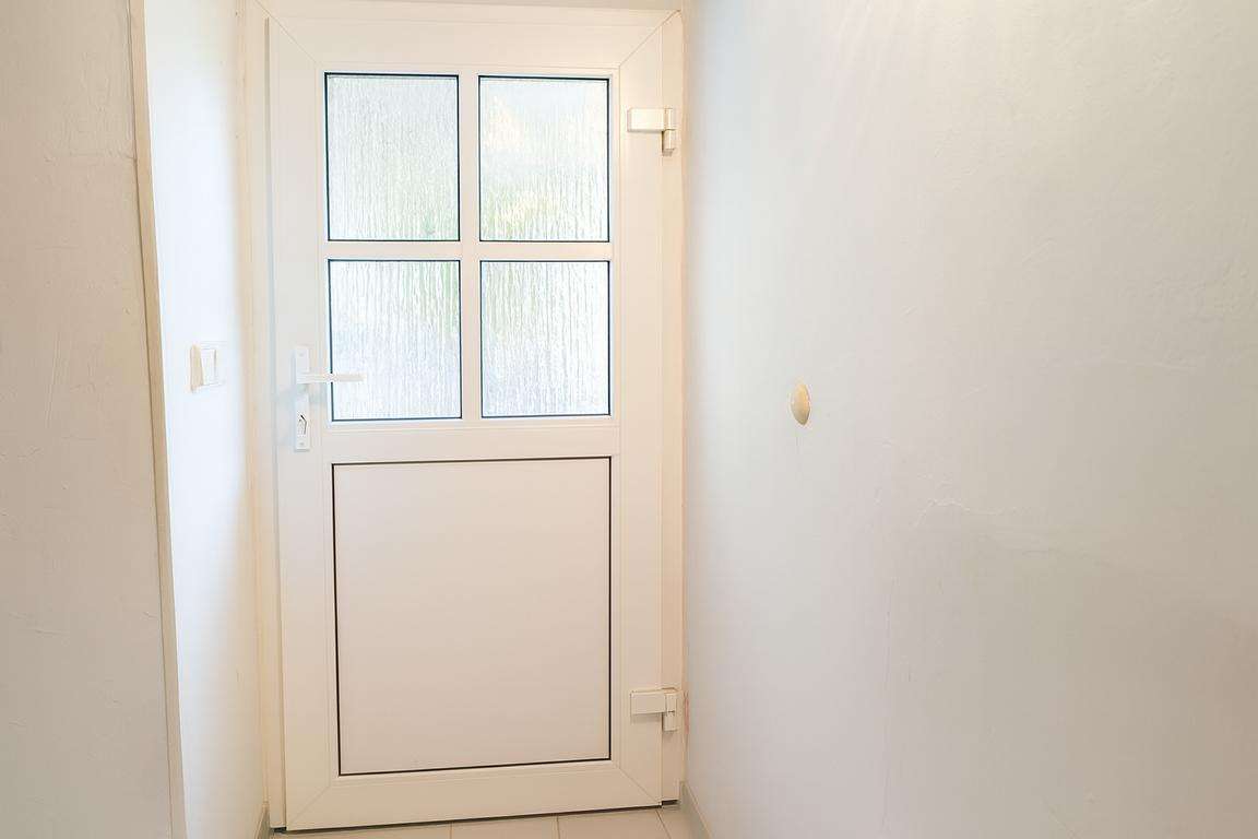 White door with four frosted-glass panels at the end of a narrow hallway; a light switch on the left wall and a small hole/dent on the right wall.