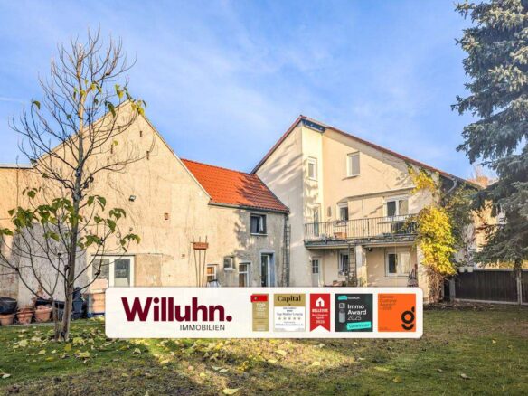Residential buildings with a red-tiled roof and a large Willuhn Immobilien sign in a green yard.