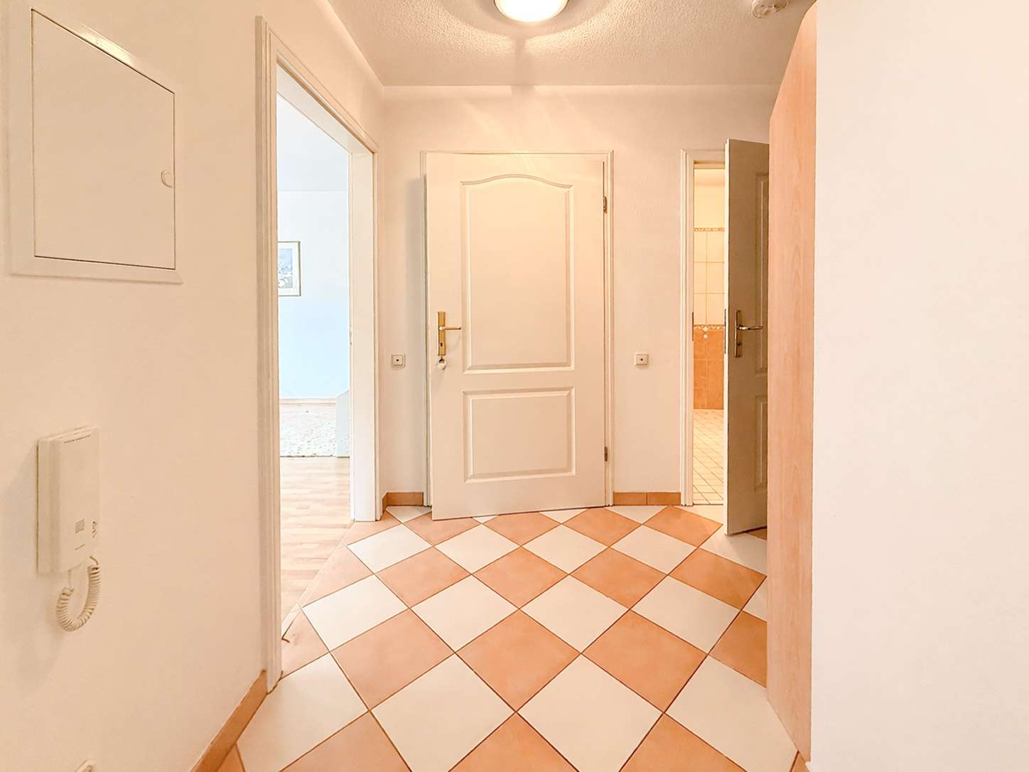 Bright hallway with white walls, open doors, and a peach-and-white checkered tile floor leading to adjacent rooms.
