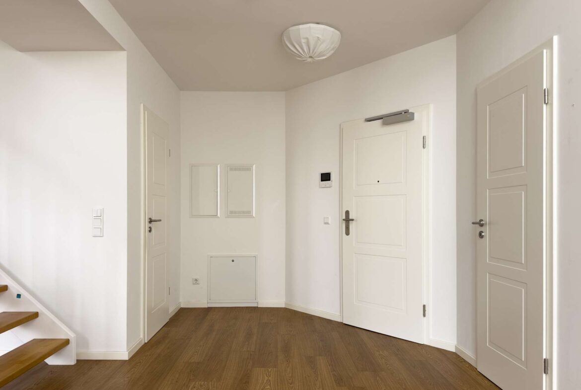 White, modern entry hall with paneled doors, light wood flooring, and a staircase to the left.