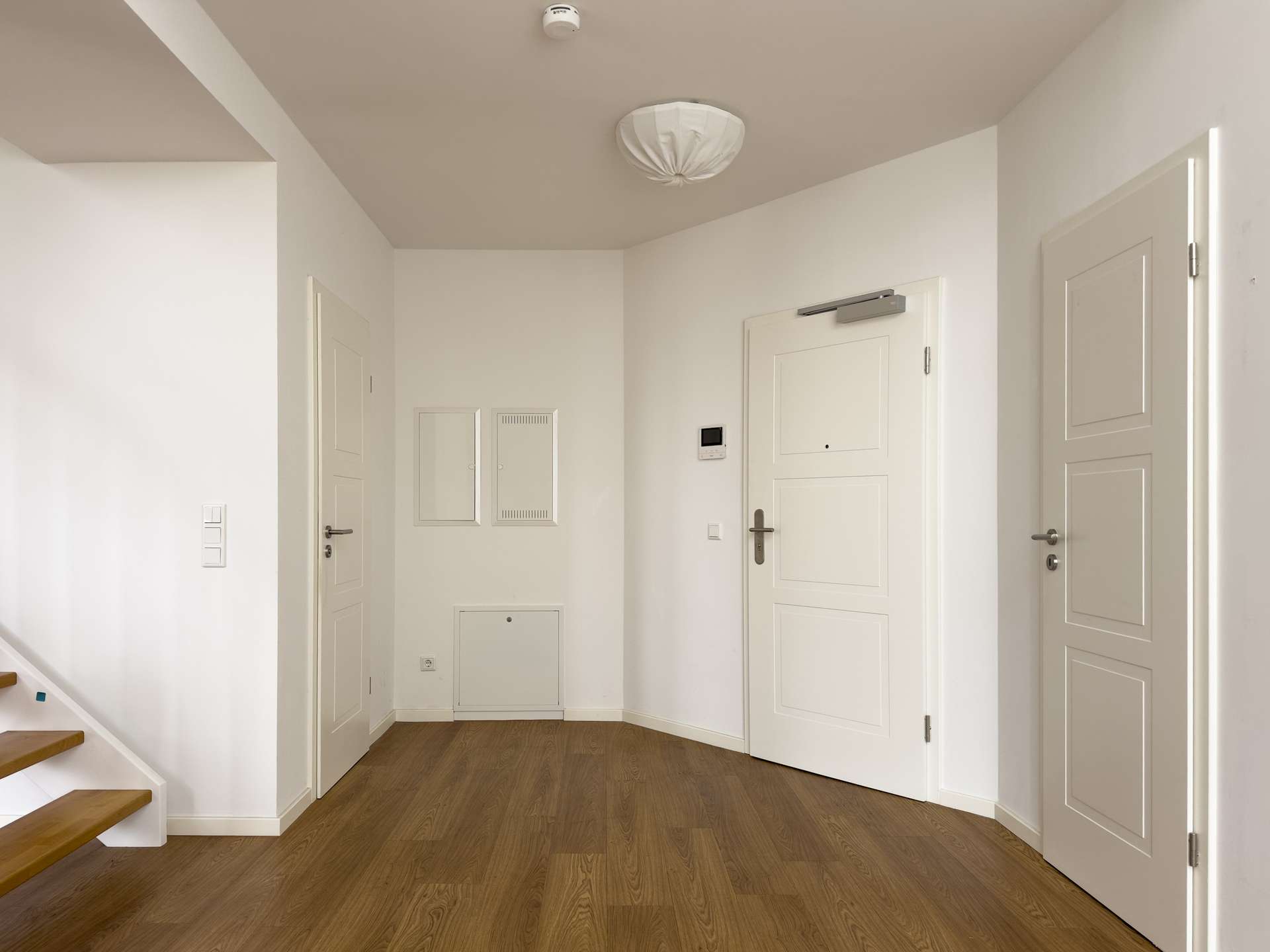 White, modern entry hall with paneled doors, light wood flooring, and a staircase to the left.