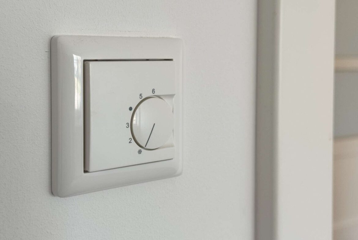 White wall thermostat close-up with a circular dial set near 4 on the scale.