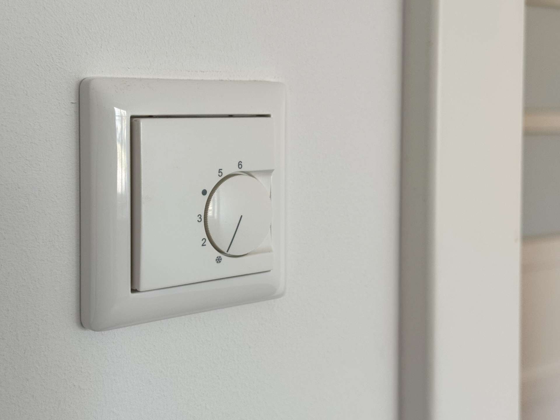 White wall thermostat close-up with a circular dial set near 4 on the scale.