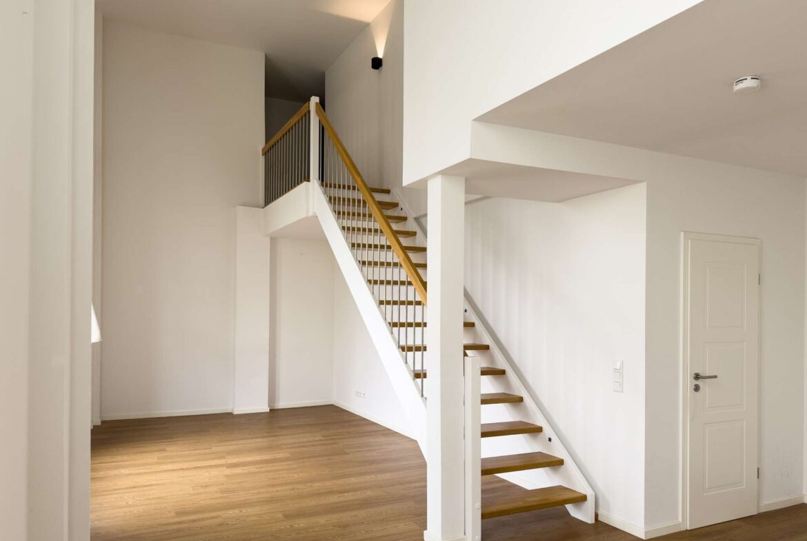 Interior stairwell with white walls and a wooden staircase leading upstairs, bright and minimal in a modern home