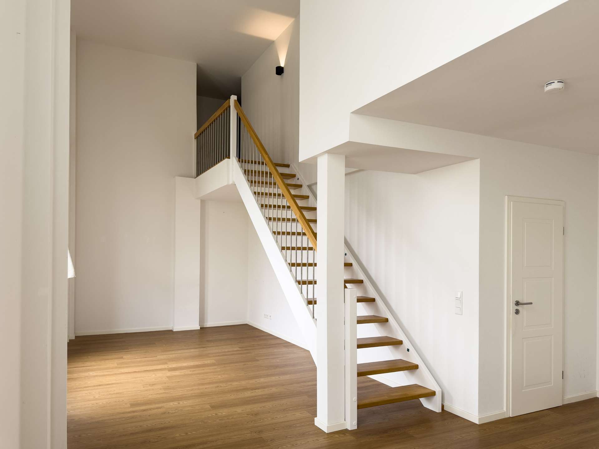 Interior stairwell with white walls and a wooden staircase leading upstairs, bright and minimal in a modern home