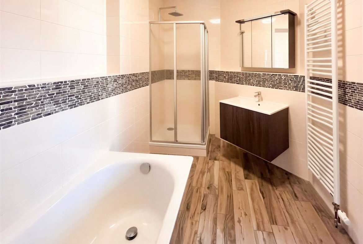 Bright contemporary bathroom with a glass shower enclosure, white tiled walls with a dark mosaic band, and a dark wood vanity.