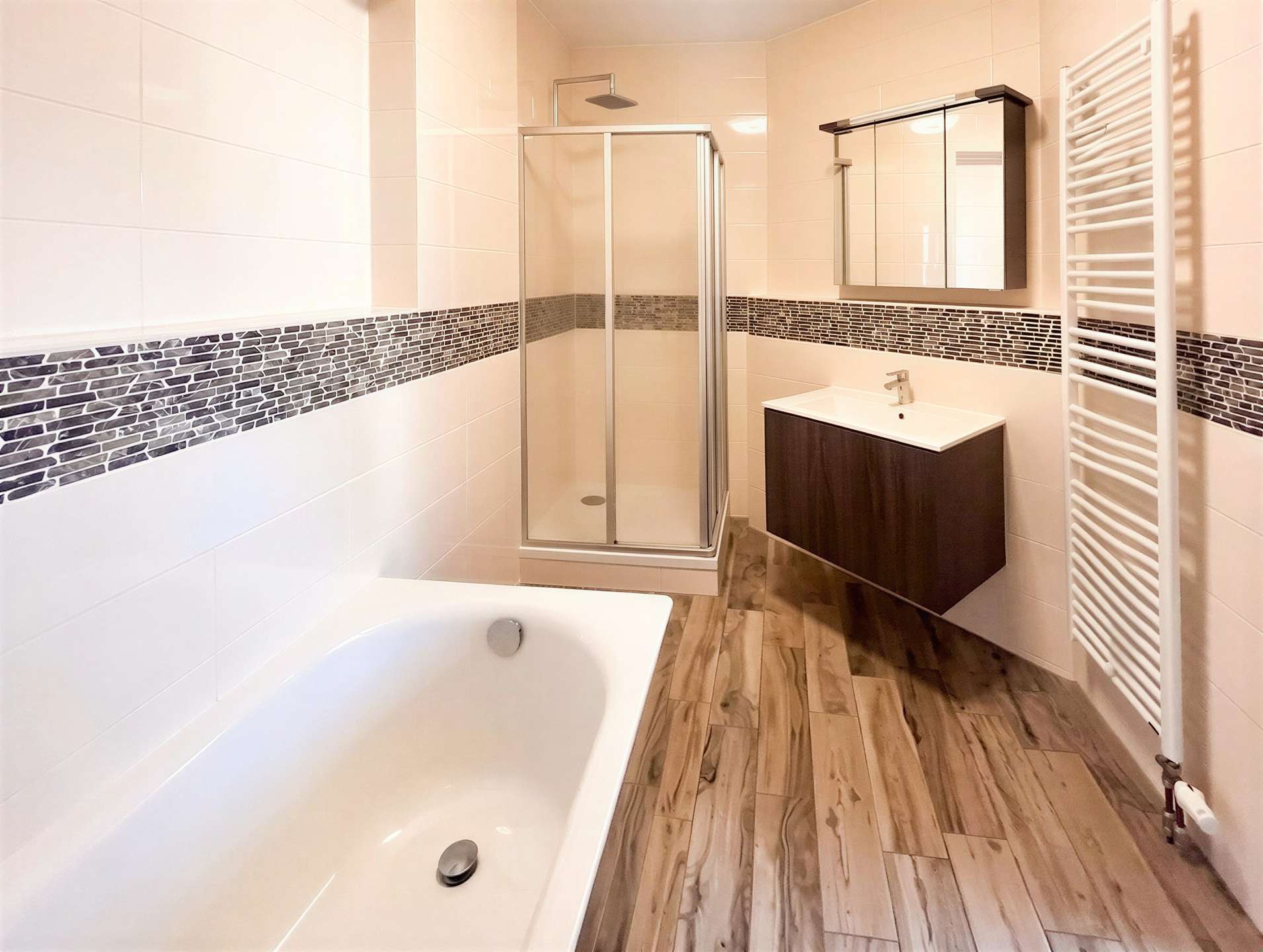 Bright contemporary bathroom with a glass shower enclosure, white tiled walls with a dark mosaic band, and a dark wood vanity.