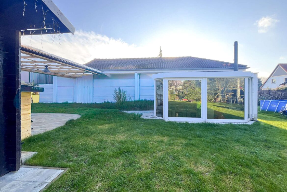 Backyard scene with a white-framed glass conservatory and a green lawn under a clear blue sky.