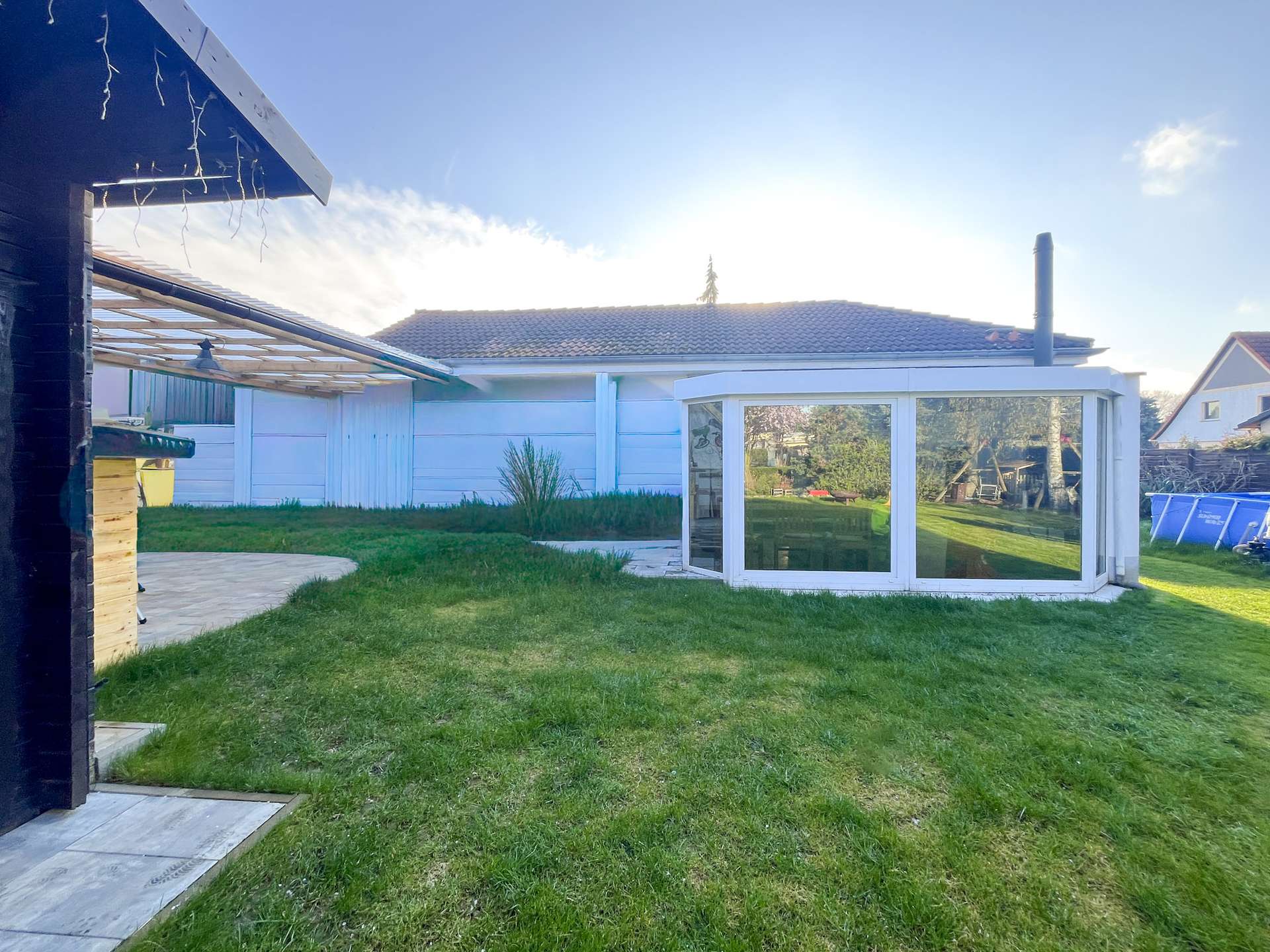 Backyard scene with a white-framed glass conservatory and a green lawn under a clear blue sky.