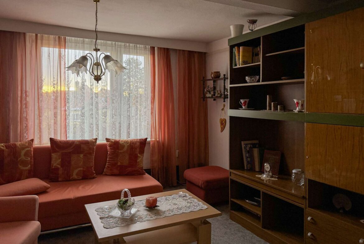 Cozy living room with pink sofa, patterned cushions, and sheer pink curtains by a large window.
