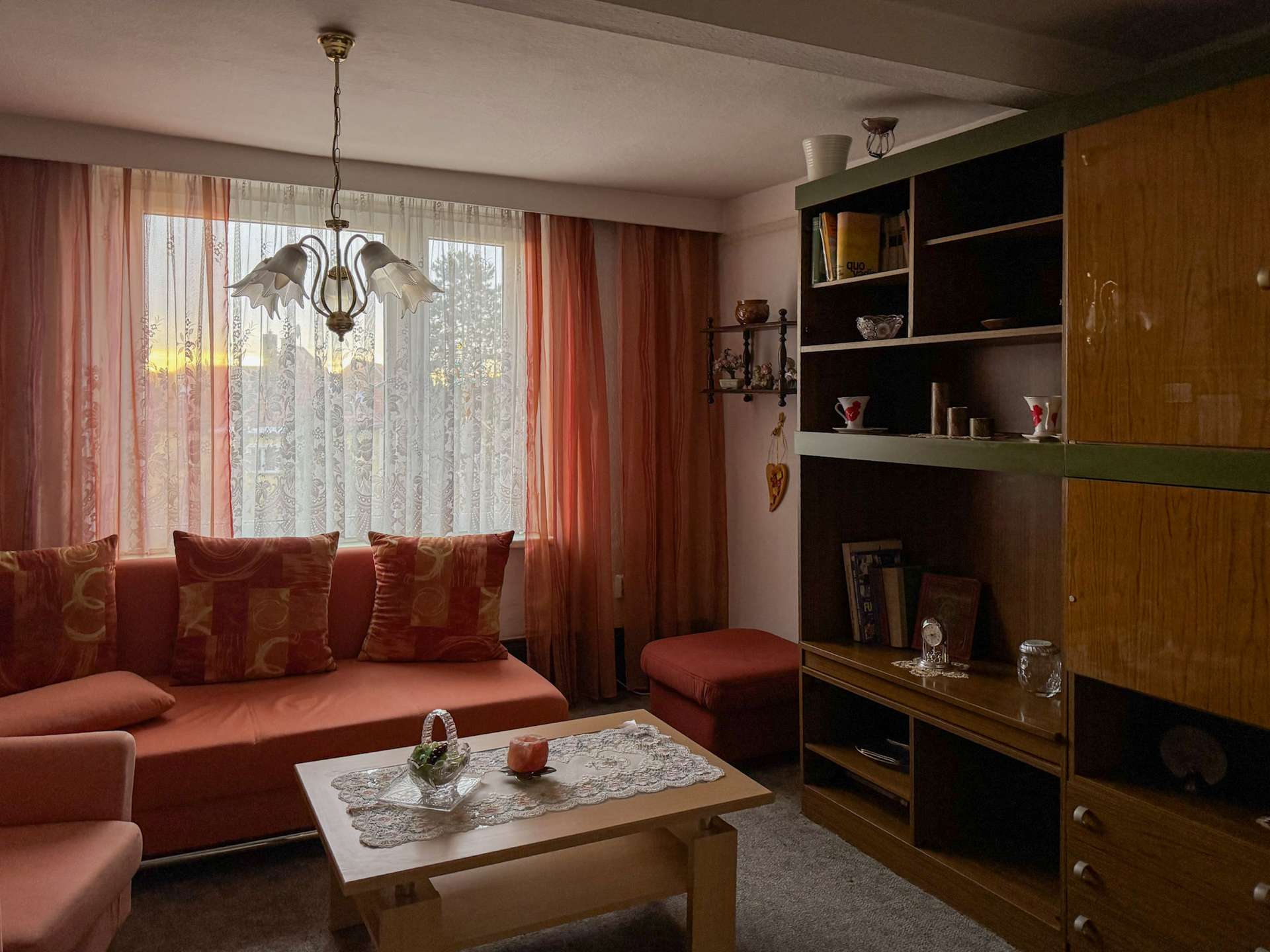 Cozy living room with pink sofa, patterned cushions, and sheer pink curtains by a large window.