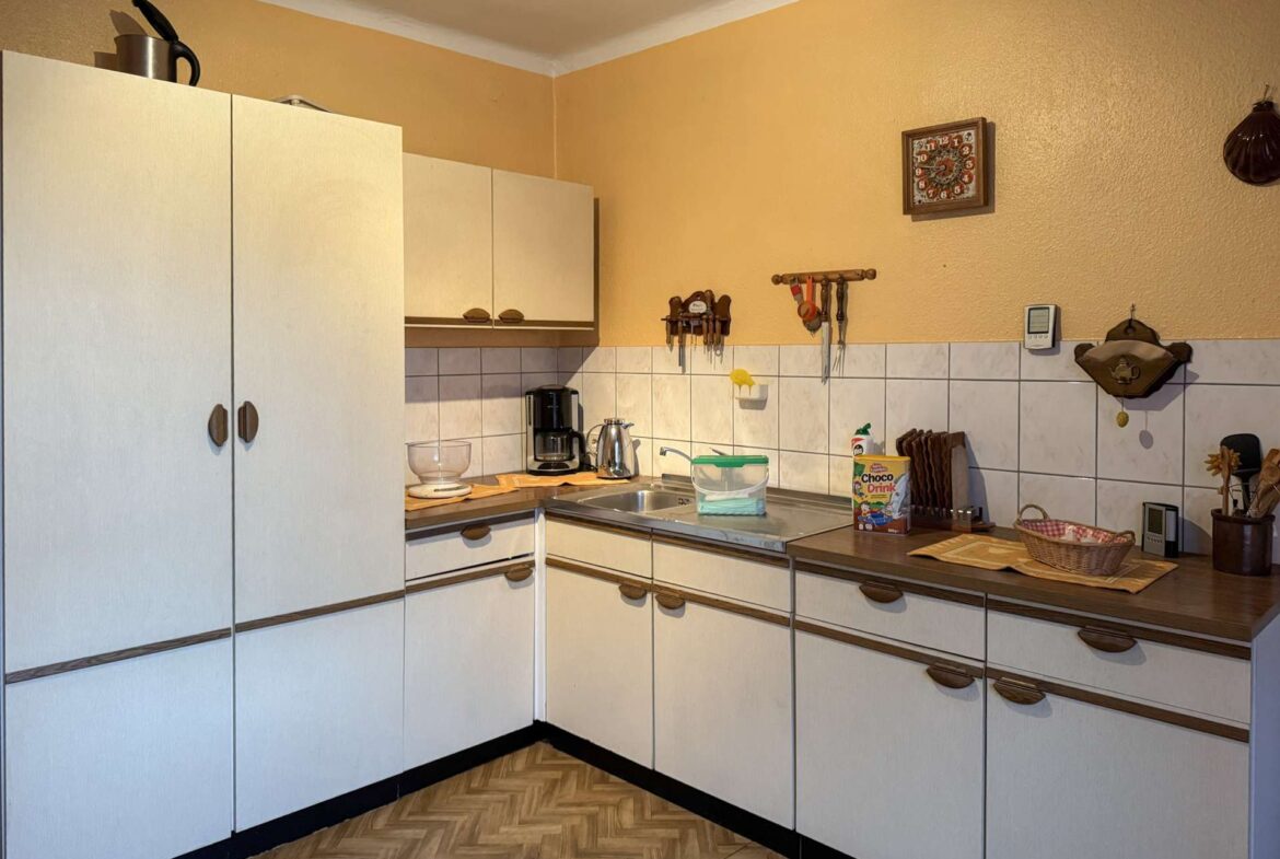 A L-shaped kitchen with white cabinets, beige walls, and tiled backsplash; coffee maker and kettle on the counter.