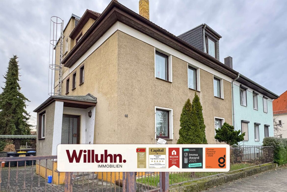 Three-story beige residential building with a large real estate sign in the foreground reading 'Willuhn Immobilien' and award stickers.