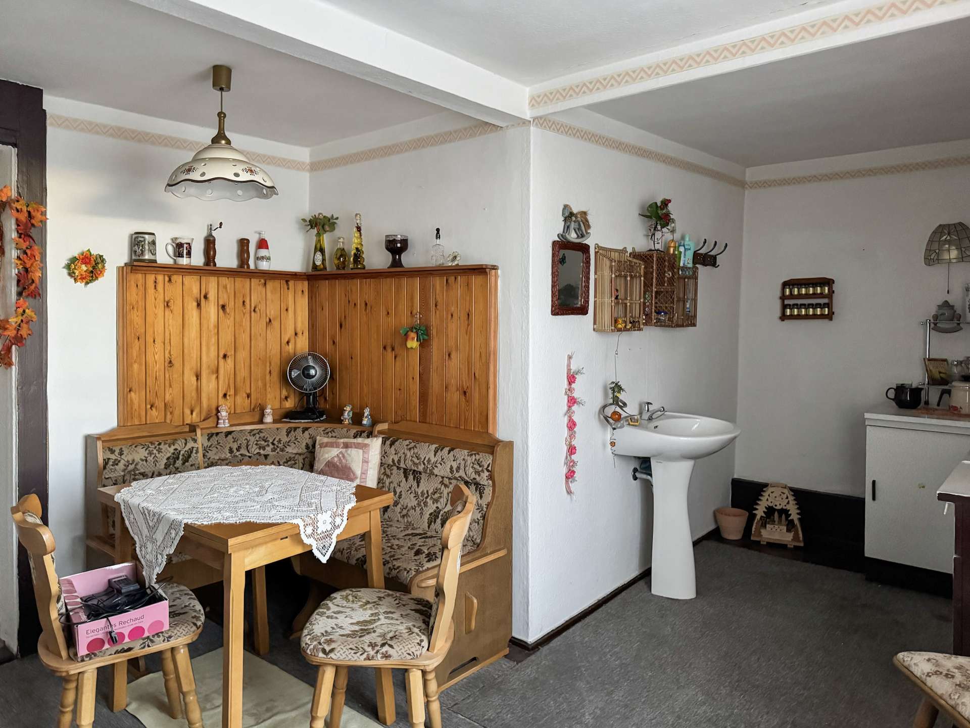 Cozy dining nook with a wooden cabinet, lace tablecloth, and floral-upholstered chairs in a vintage-style kitchen area of a home.