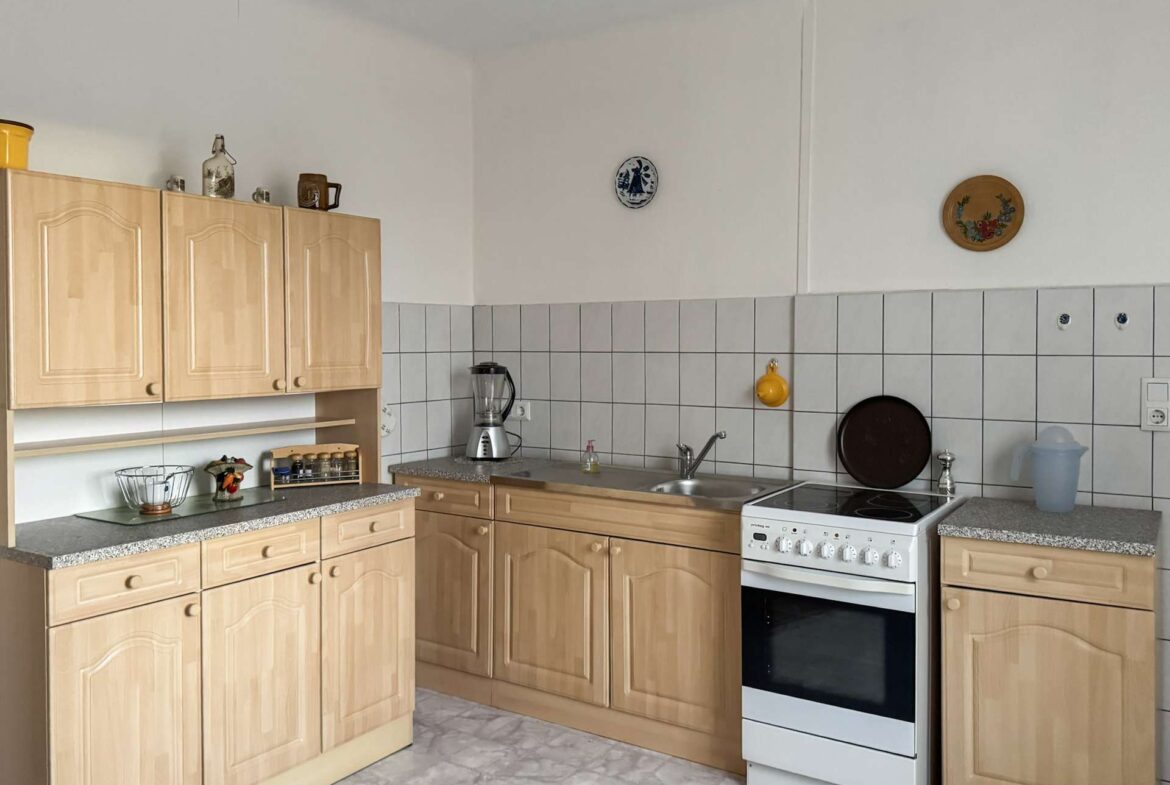 Kitchen with light wood cabinets, tiled backsplash, sink, and a white oven set in a U-shaped counter layout