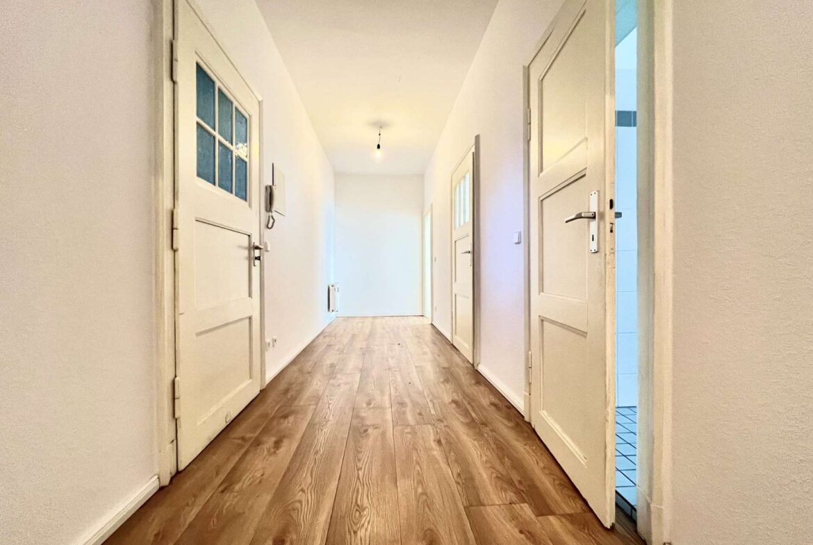 Narrow white hallway with paneled doors on both sides and a single bare lightbulb.