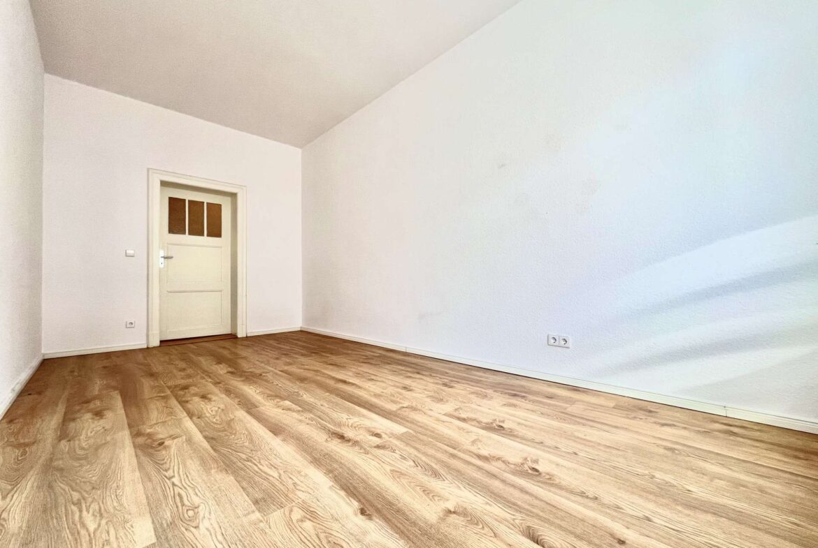 Room with white walls, light wood plank flooring, and a white door in the back left corner.