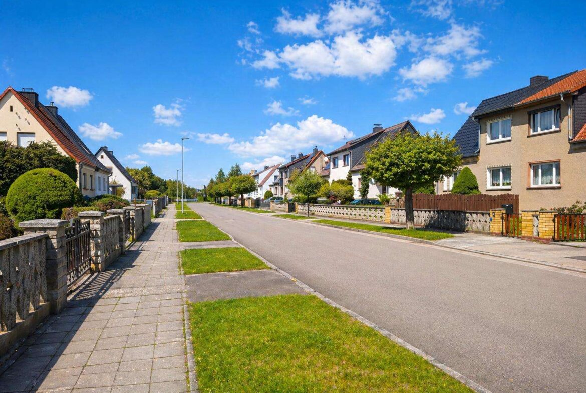 Suburban street with row houses, manicured lawns, and a blue sky.