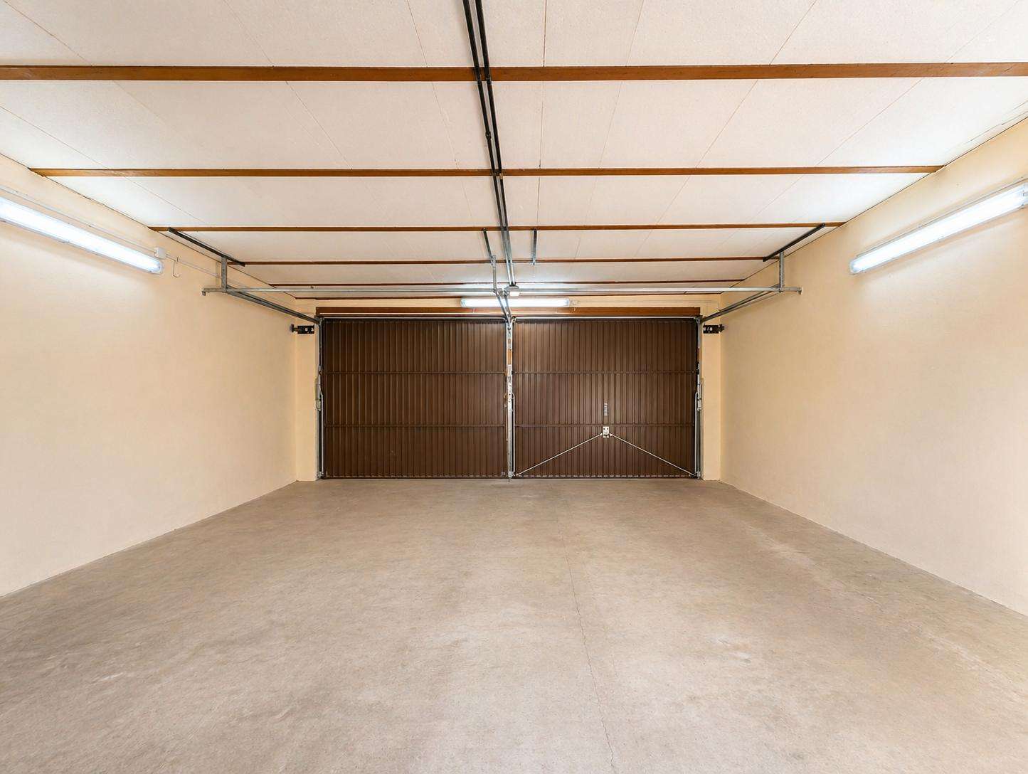 Empty two-car garage with brown sectional doors, concrete floor, and bright fluorescent lighting.