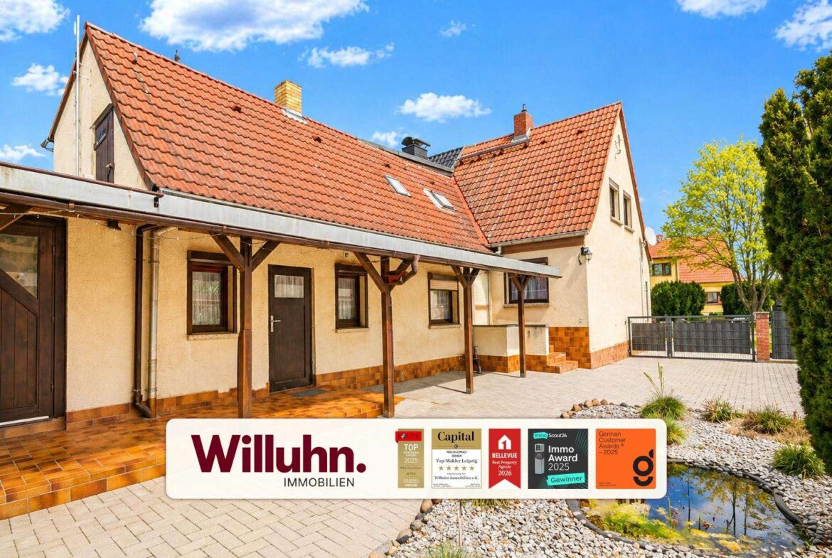 Front view of a beige house with red-tiled roof and a long covered walkway, Willuhn Immobilien banner across the bottom.