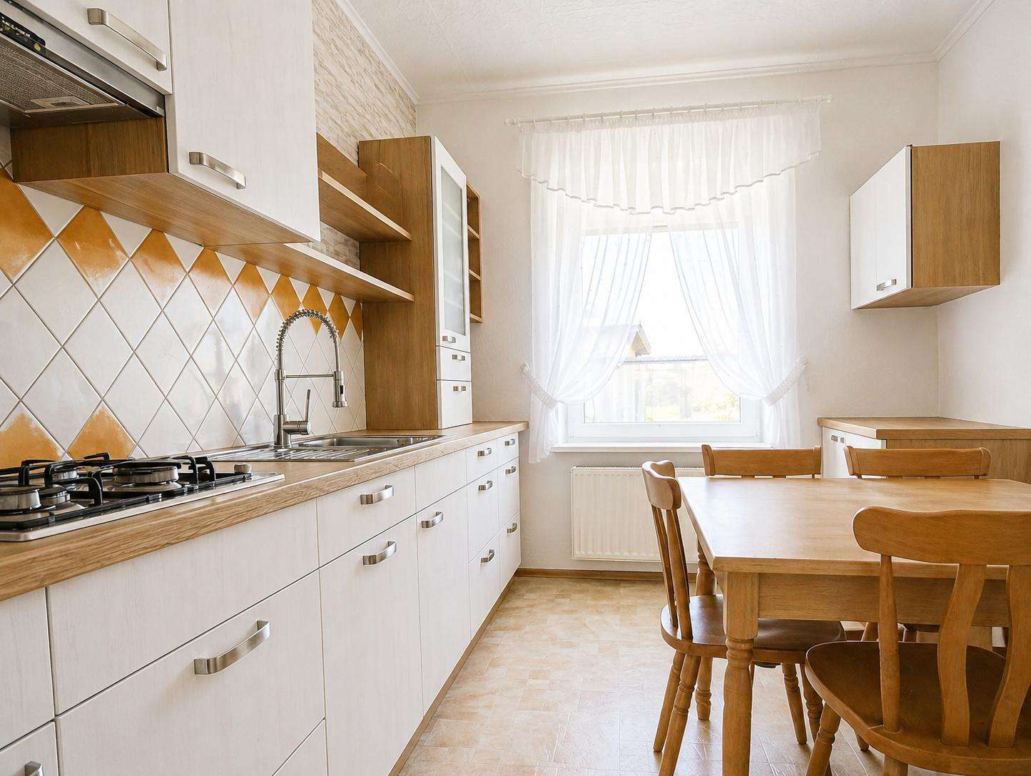 Bright kitchen with white cabinets, orange diamond tile backsplash, stainless sink, and a wooden dining table by a window.