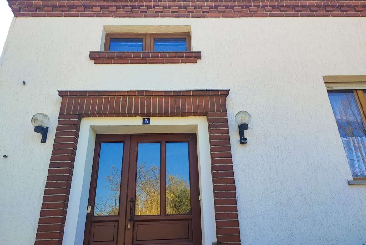 Front door with brown wood panels framed by red brick and white stucco, number 5, with two wall lamps.