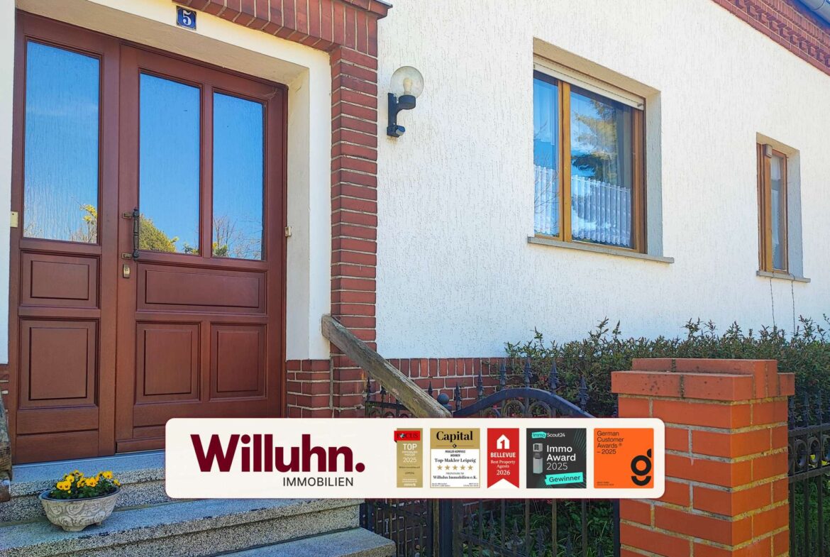 Residential building facade with red brick trim, brown wooden double doors, and a large white real estate banner reading 'Willuhn Immobilien' across the lower portion with award stickers.