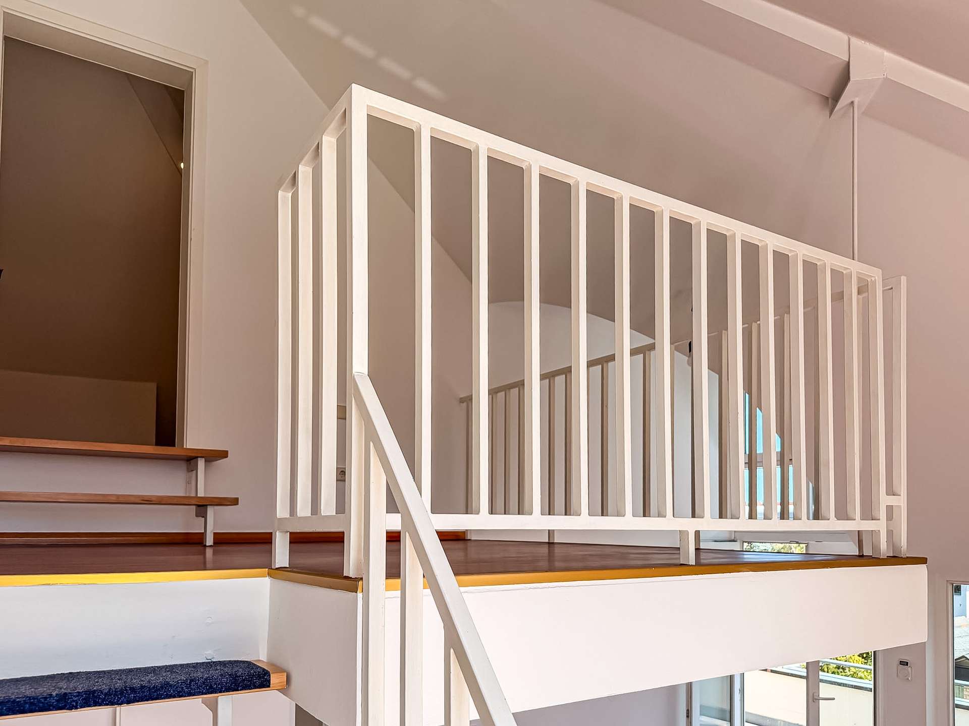 Indoor stairwell with white vertical-bar railing and wood steps, leading to a mezzanine balcony area.