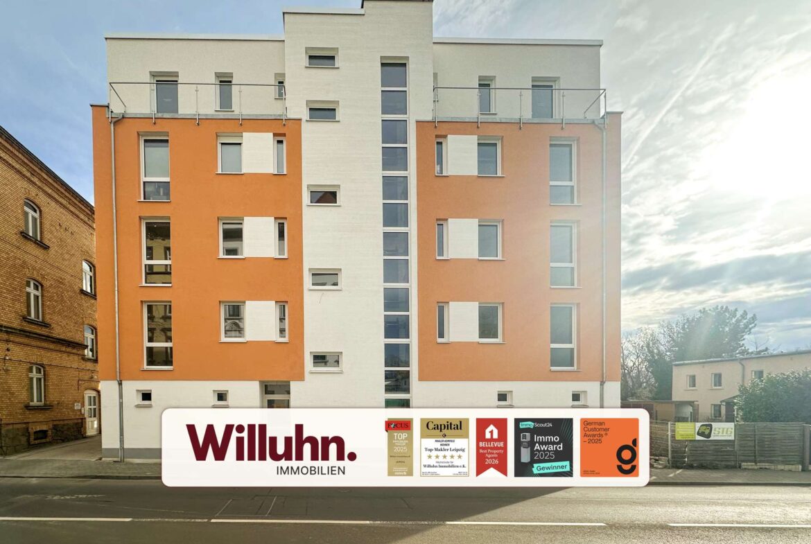 Modern orange-and-white apartment building with a large real estate banner at street level outside the entrance area.