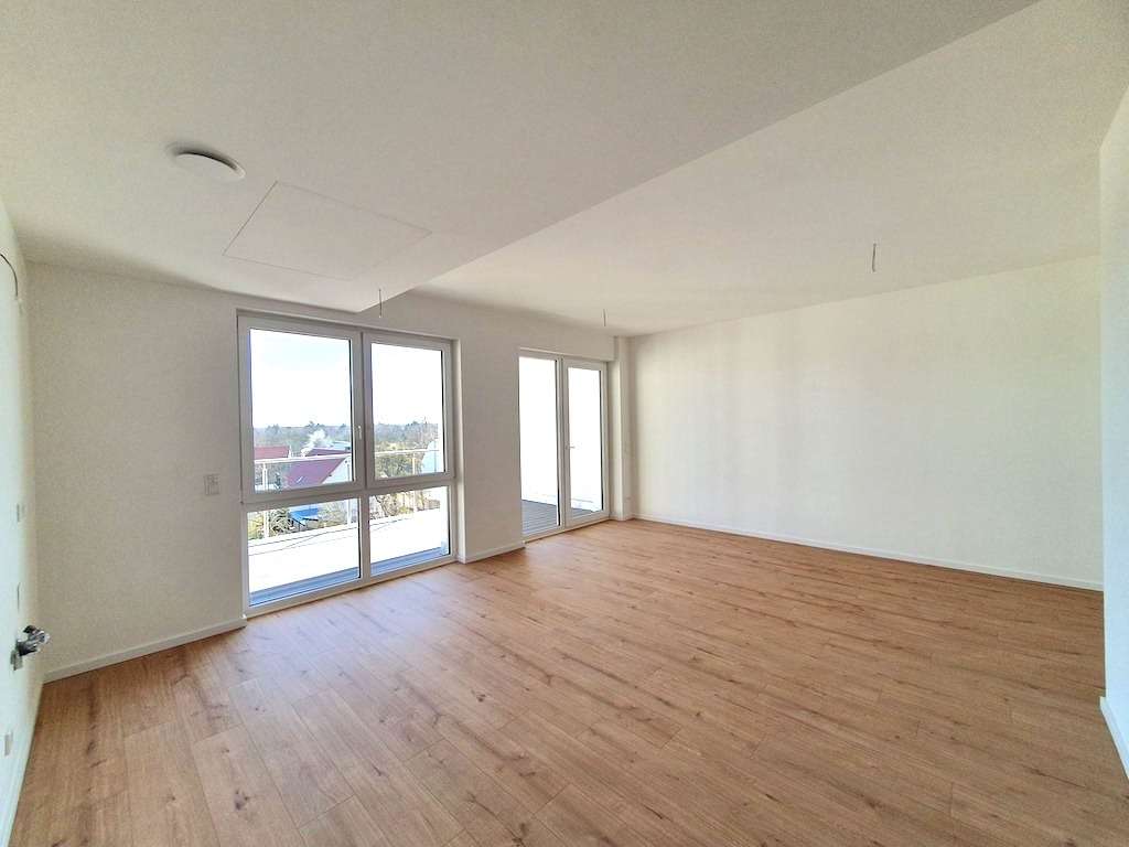 Bright, empty living room with light wood flooring and large glass windows bringing in ample natural light.
