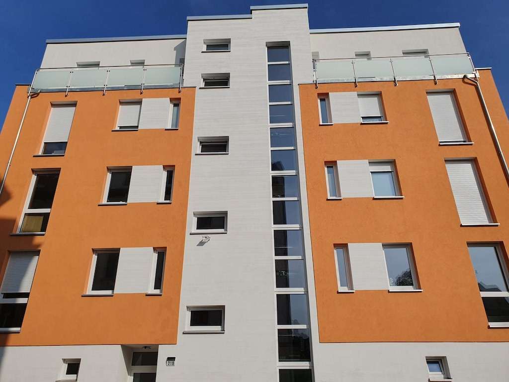 Front view of a modern multi-story apartment building with orange exterior walls and a white central column featuring tall windows.