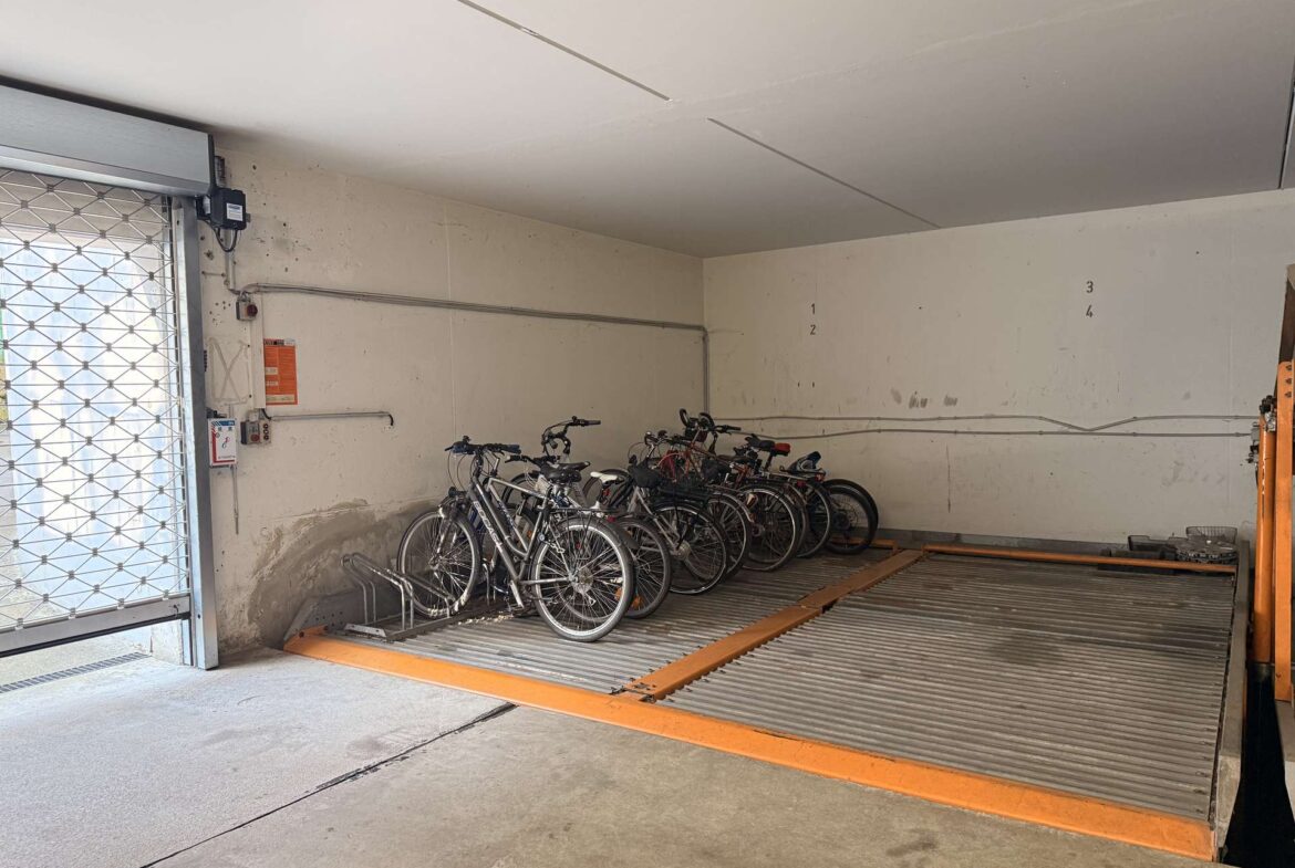 Indoor bike storage area with multiple bicycles parked along a wall and an orange safety ramp in the foreground.