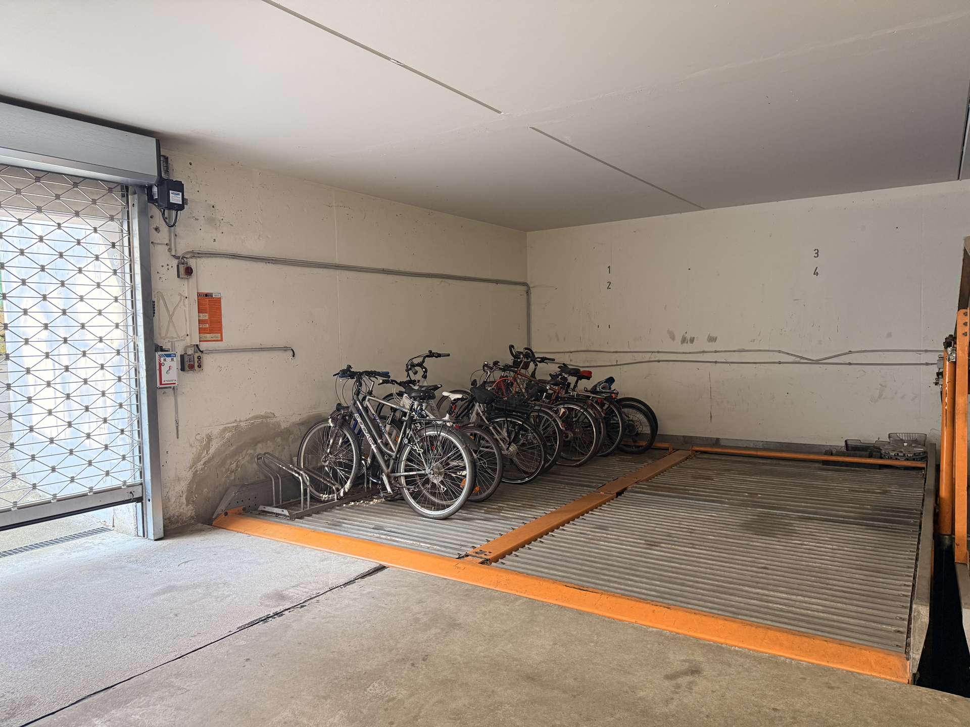 Indoor bike storage area with multiple bicycles parked along a wall and an orange safety ramp in the foreground.