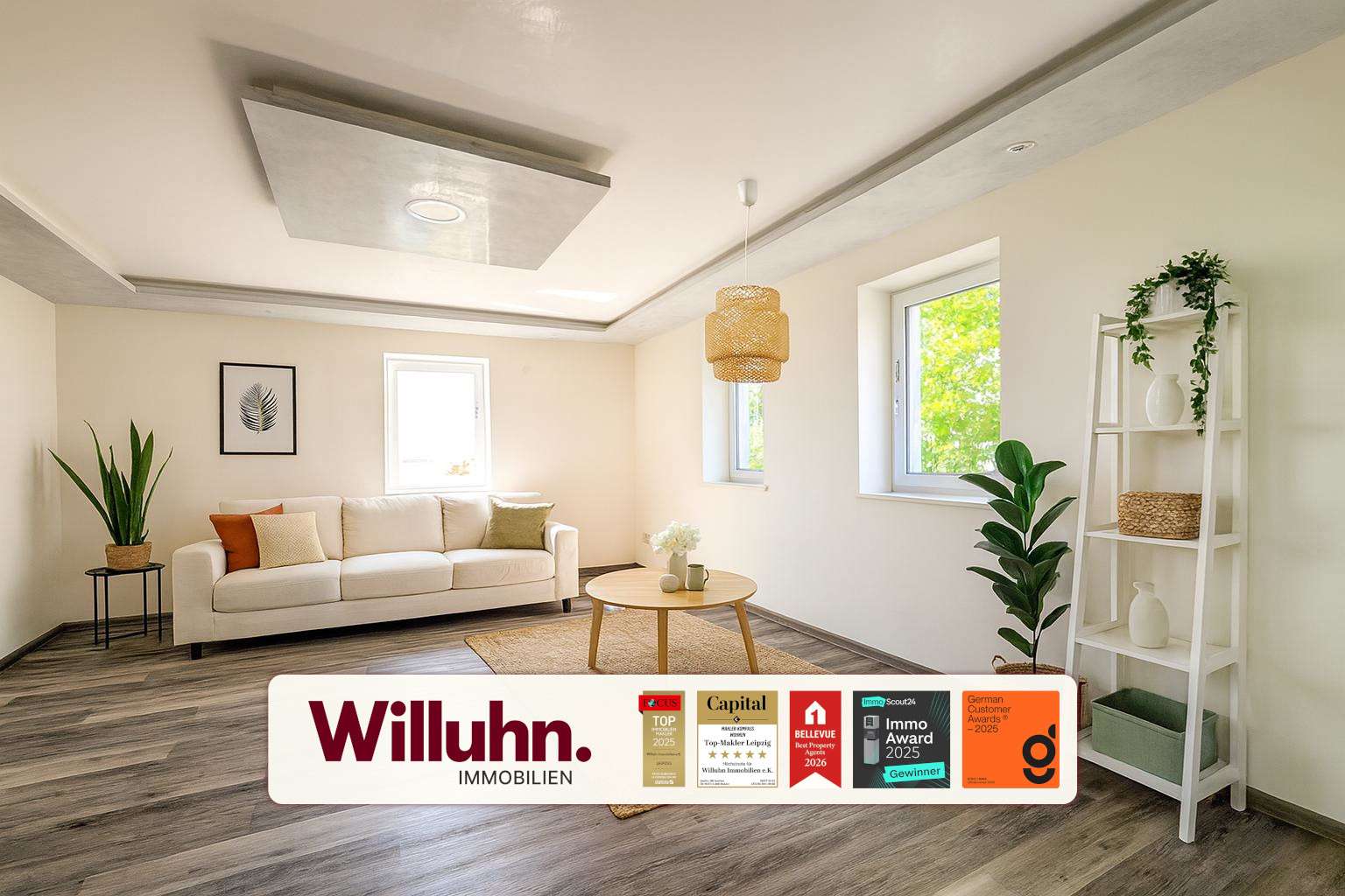 Bright living room with a white sofa, round wooden coffee table, and tall green plants; Willuhn Immobilien branding banner at the bottom.