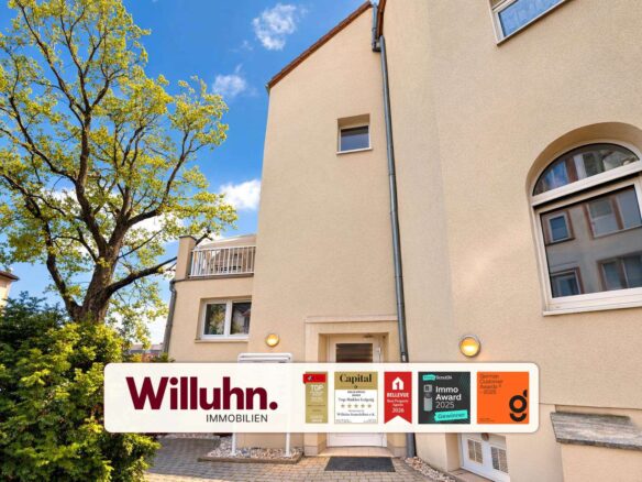 Beige residential building with a large tree on the left and a white Willuhn Immobilien banner with awards across the bottom edge.