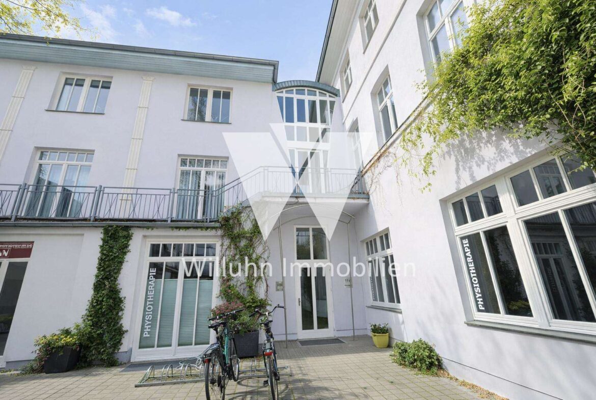 White clinic building with large windows, a glass atrium, ivy on the wall, and bicycles outside.