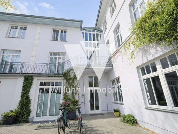 White clinic building with large windows, a glass atrium, ivy on the wall, and bicycles outside.