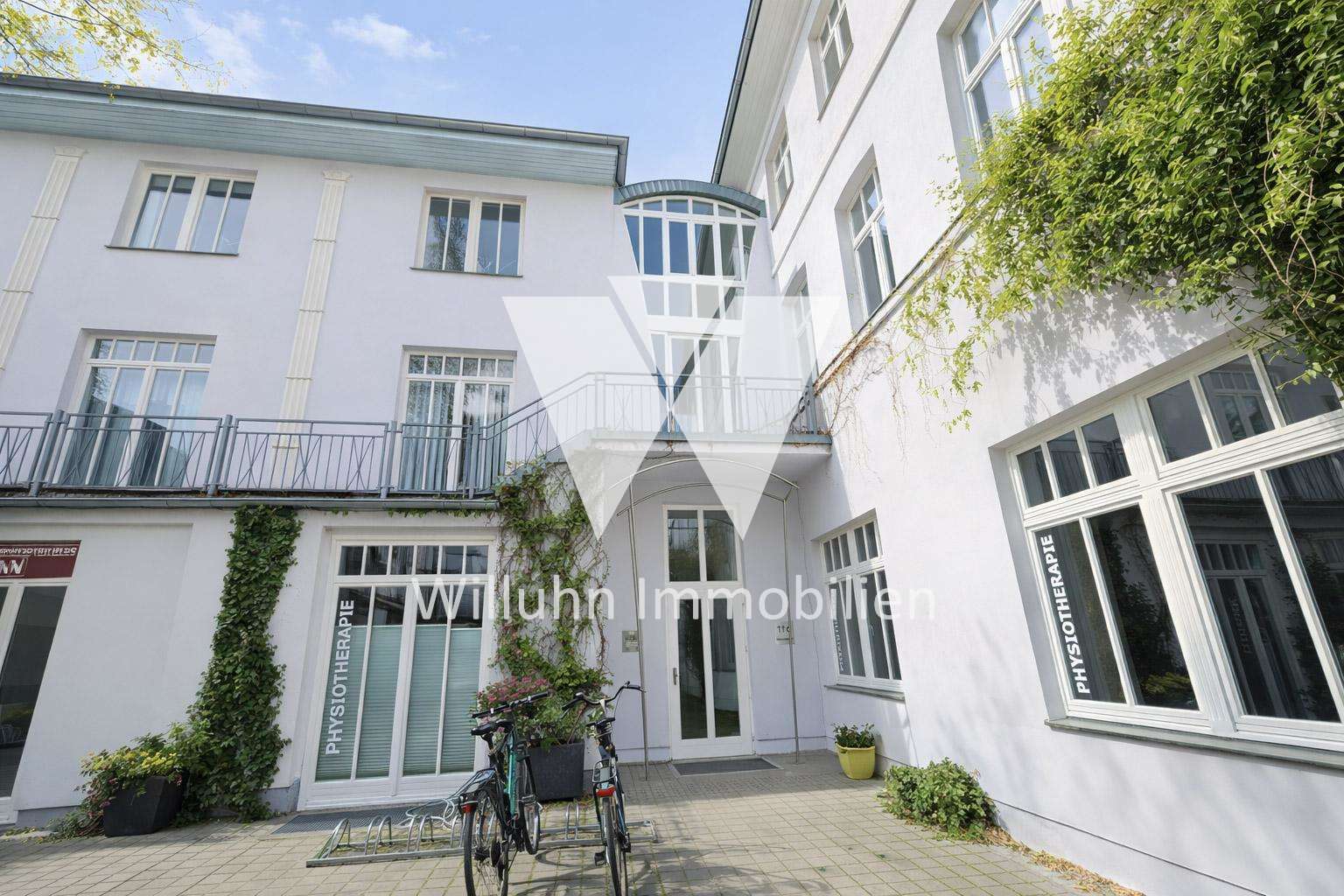 White clinic building with large windows, a glass atrium, ivy on the wall, and bicycles outside.