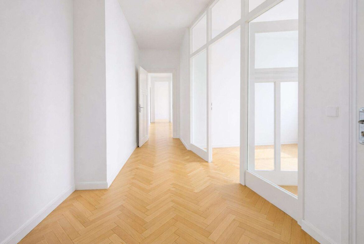 Bright white hallway with tall glass-paneled doors on the right and a light herringbone wooden floor