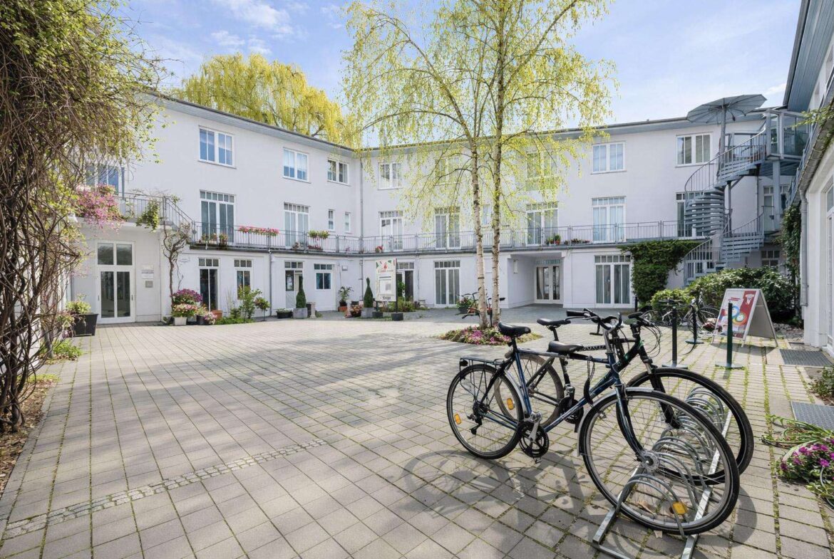 Courtyard of a white multi-story building with bicycles docked at a rack and potted plants along the walls.